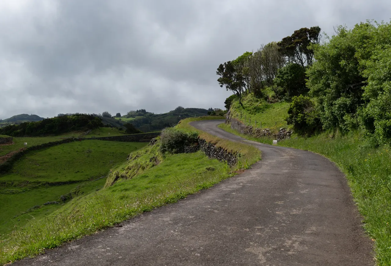 A narrow country road curving between green pastures and stone walls on Santa Maria under a cloudy sky
