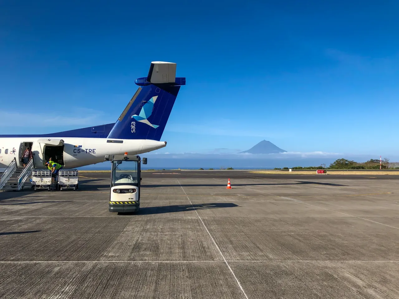 A SATA Dash 8 airliner parked at São Jorge Airport with the cone of Mount Pico rising behind it