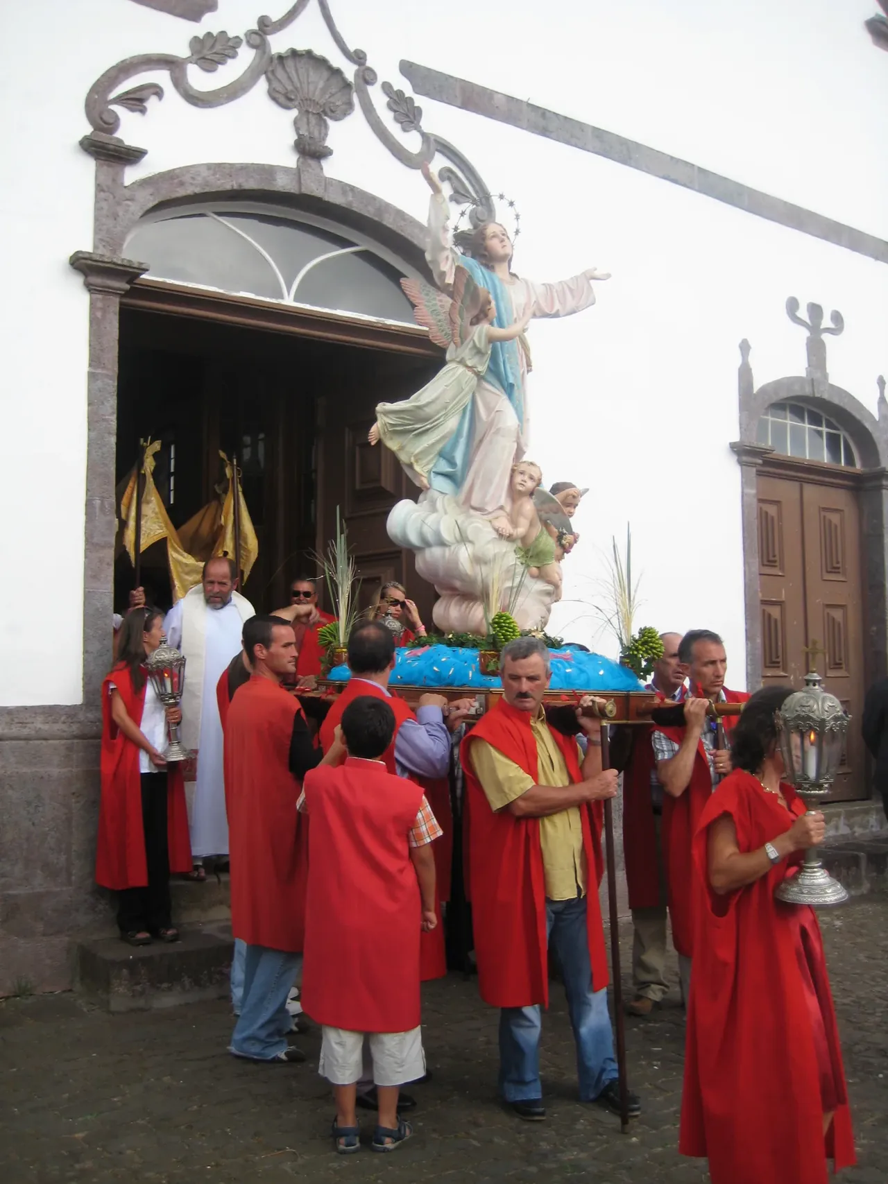 Des hommes en capes rouges portent une statue de Notre-Dame de l’Assomption hors d’une église blanche de Vila do Porto