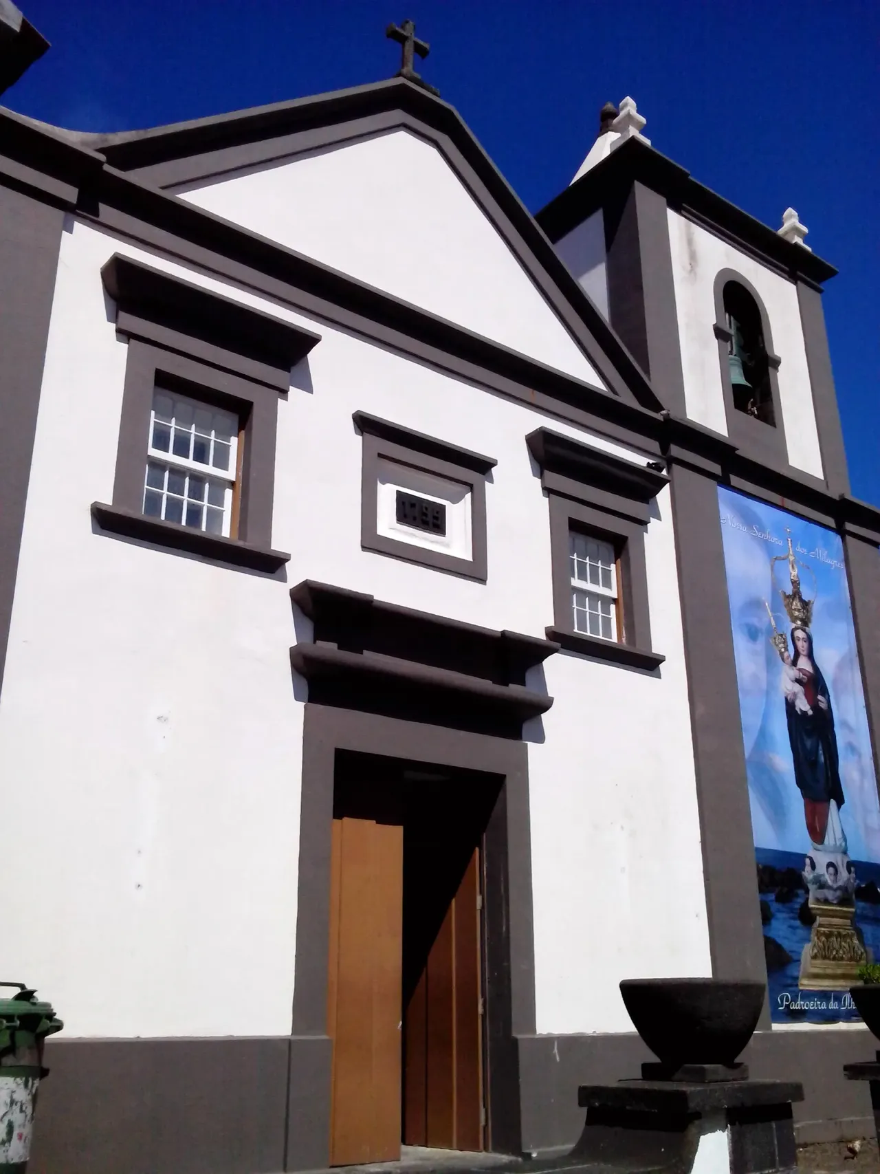 Die weiße Kirche Nossa Senhora dos Milagres in Vila do Corvo mit einem Marienbanner neben der Tür