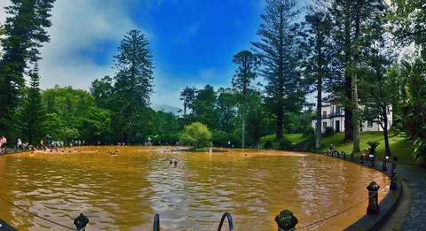 Bagnanti nella grande piscina termale bruno-arancio del Parque Terra Nostra a Furnas, circondata da alti alberi