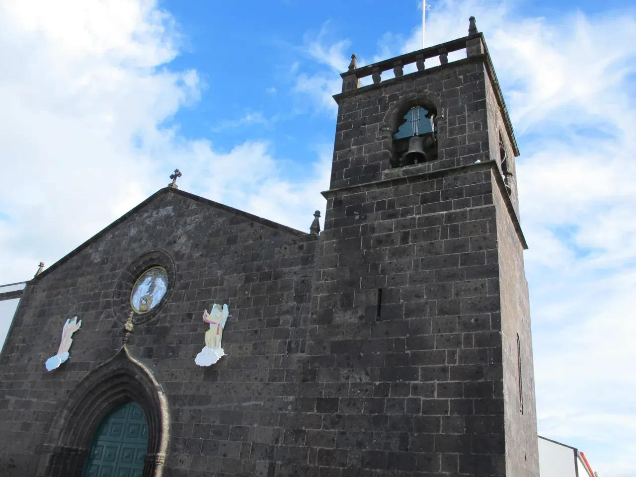 La façade en pierre sombre et le clocher de l’église São Miguel Arcanjo à Vila Franca do Campo, sous un ciel bleu
