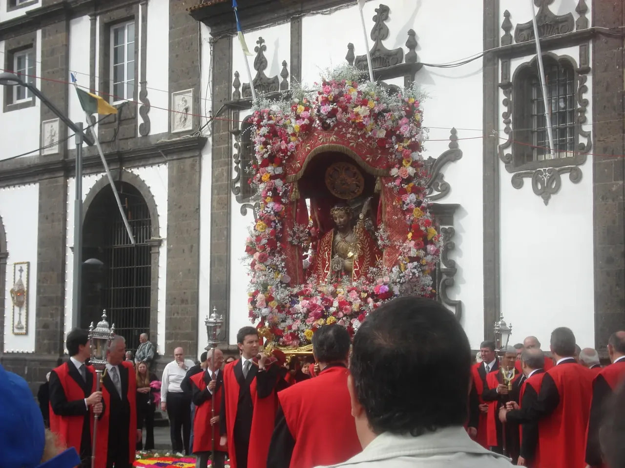 Das blumengeschmückte Bildnis des Senhor Santo Cristo wird von Männern in roten Umhängen aus dem Convento da Esperança getragen