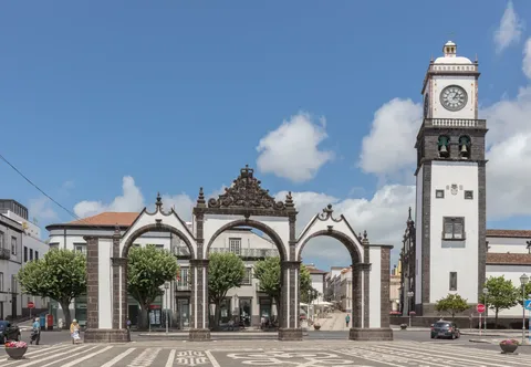 The white three-arched Portas da Cidade gates and a church bell tower in Ponta Delgada under a blue sky
